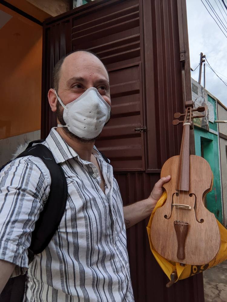 Michael Silvers, masked, holding one of the mestre's large wooden rabecas outside the house