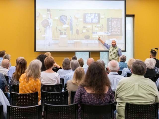 Michael Silvers pointing to a projected exhibit image before a seated audience at the Musical Instrument Museum